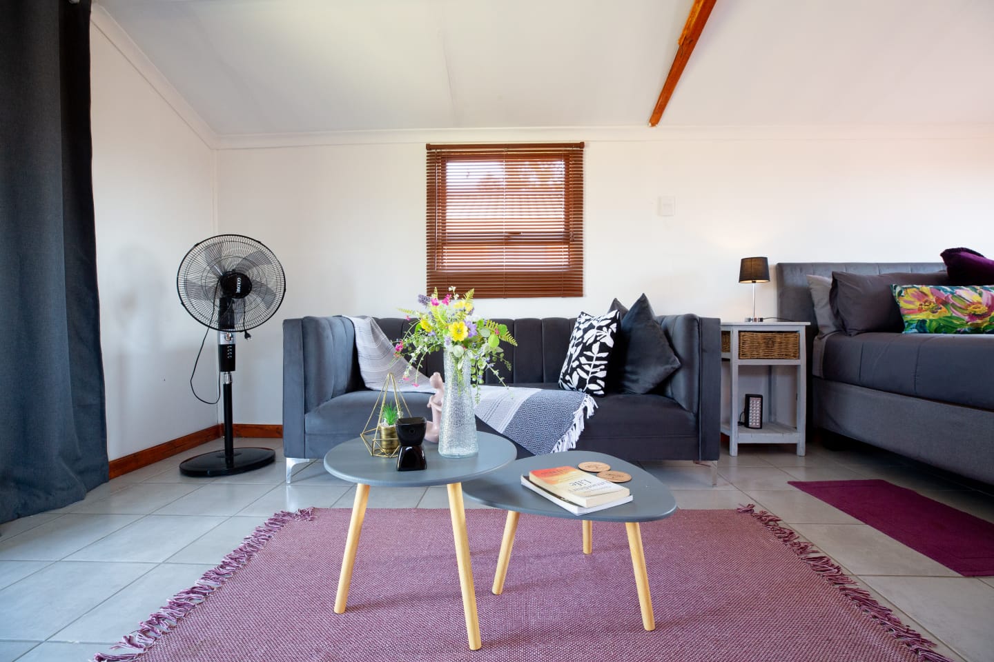 A relaxed cabin living area with a sofa, coffee tables, soft rug, flowers, and comfortable bedroom space nearby.